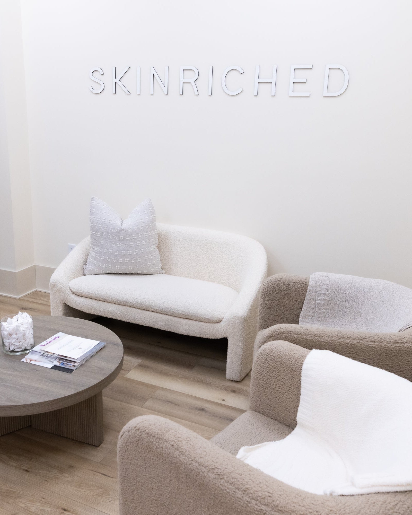 Modern living room with white sofa, armchairs, and round coffee table.